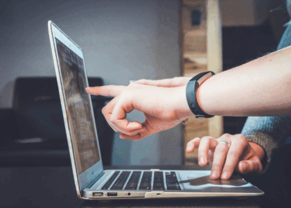 Person working on laptop at wooden desk, pointing at screen during a business meeting.