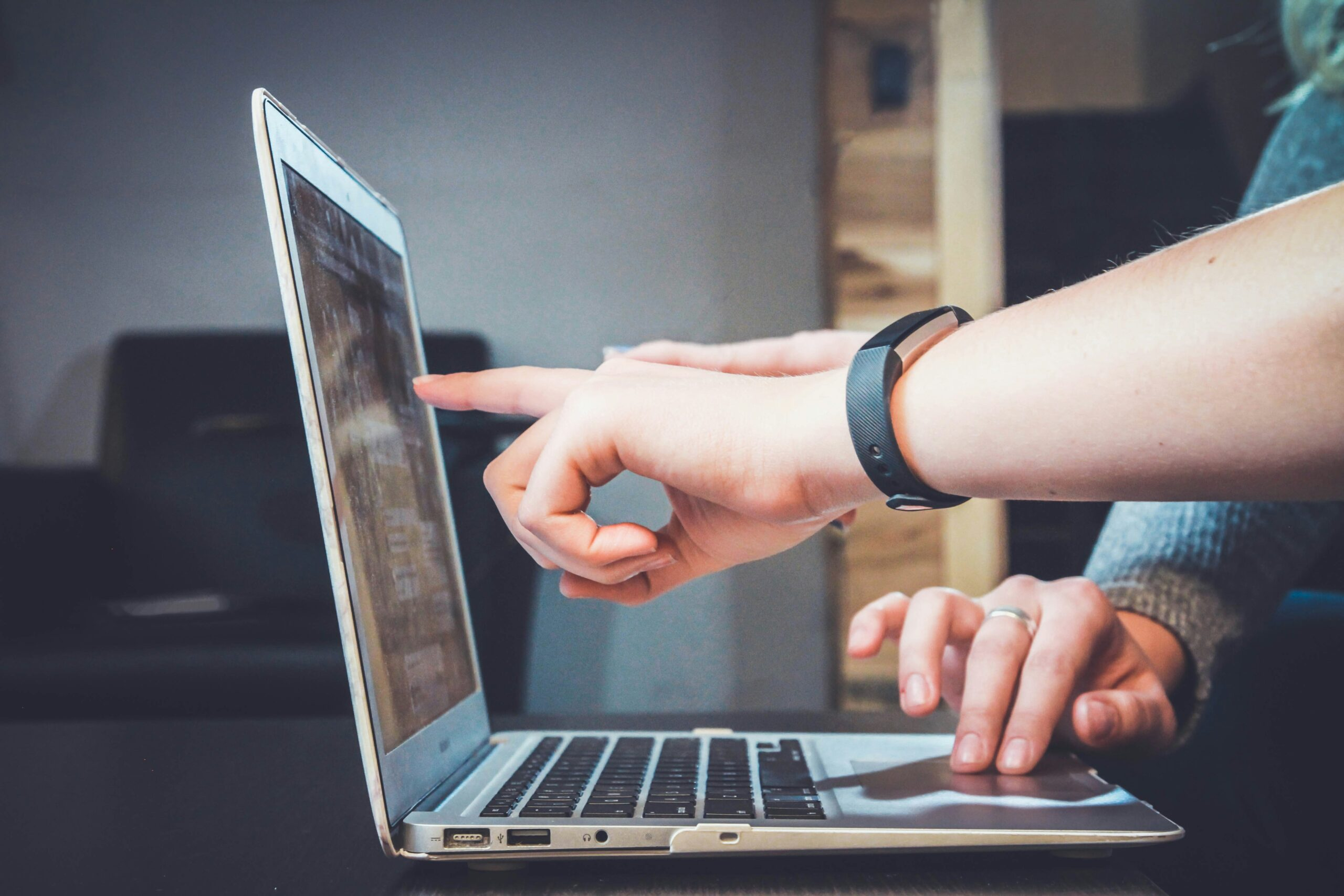 Person working on laptop at wooden desk, pointing at screen during a business meeting.