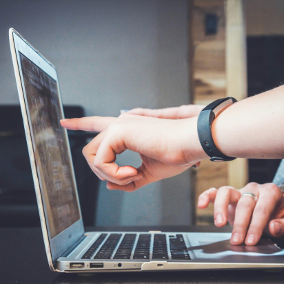 Person working on laptop at wooden desk, pointing at screen during a business meeting.